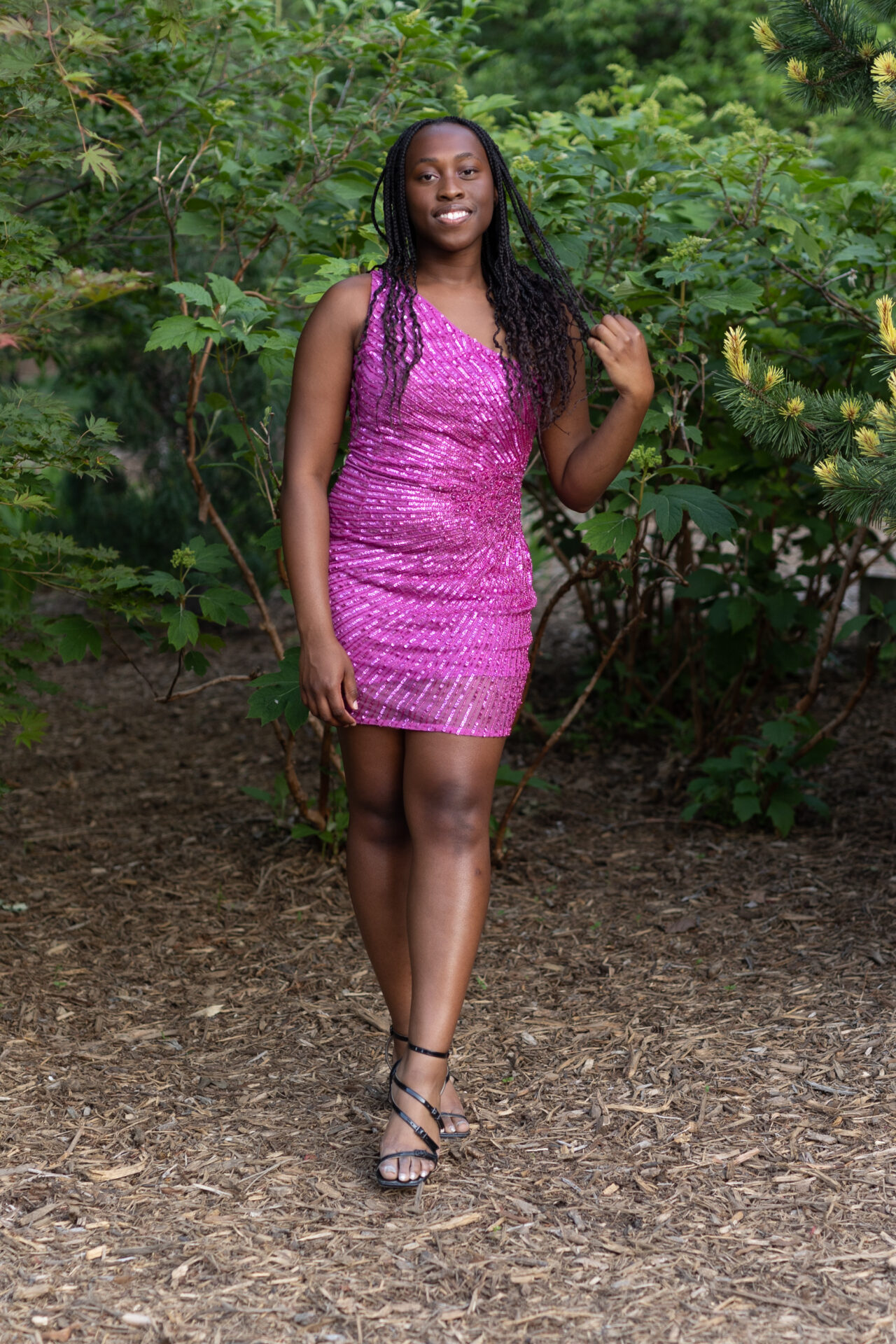 Girl in short fuchsia dress stands in front of shrub