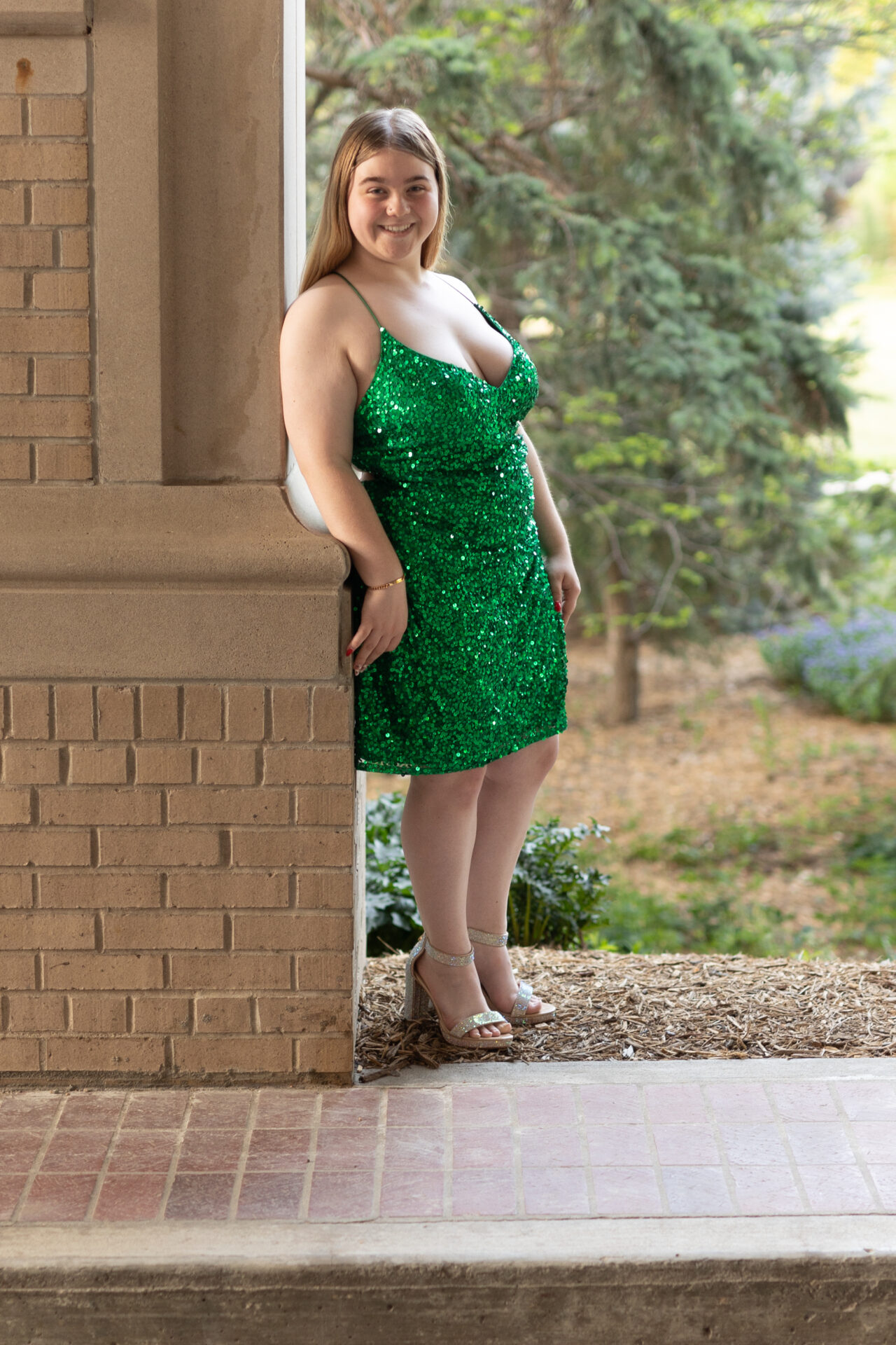 Girl in short sequined emerald dress leans against a pillar